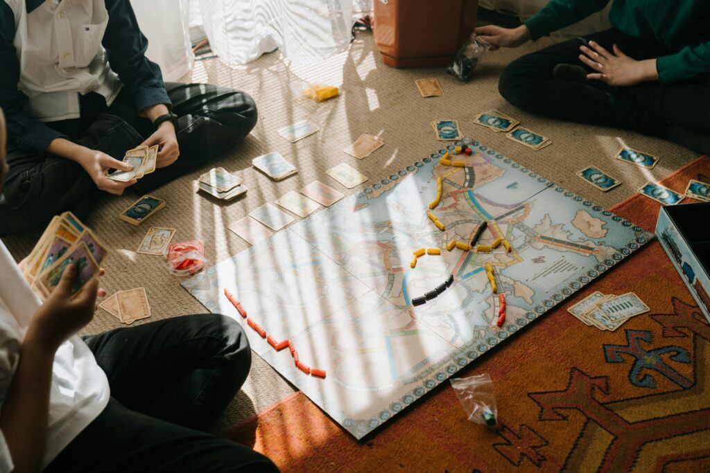 Kids enjoy a tabletop board game with map-based gameplay, cards, and tokens indoors.